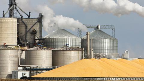 Image of grain silos and refinery with pile of corn in front