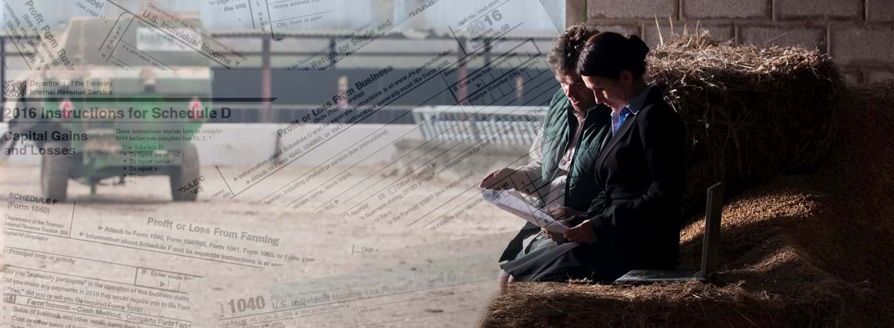 Composit image of tax forms superimposed over a woman and man reviewing documents with farm equipment in background 