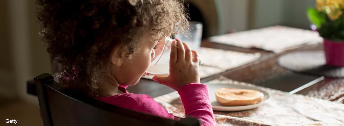 A little girl eating breakfast and drinking milk
