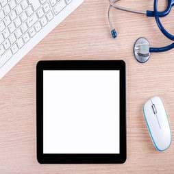 An Ipad surrounded by a white keyboard, a white mouse, and a stethoscope