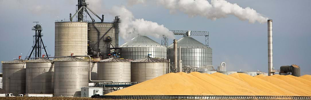 Image of grain silos and refinery with pile of corn in front.