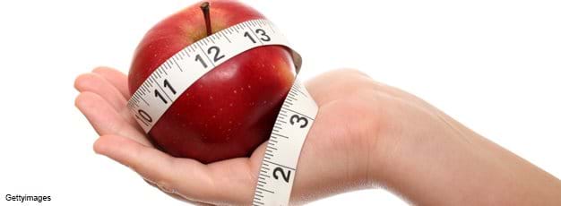 A child's hand holding an apple and measuring tape