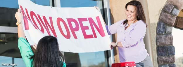 Ladies hanging "Now Open" banner over the door of their new business