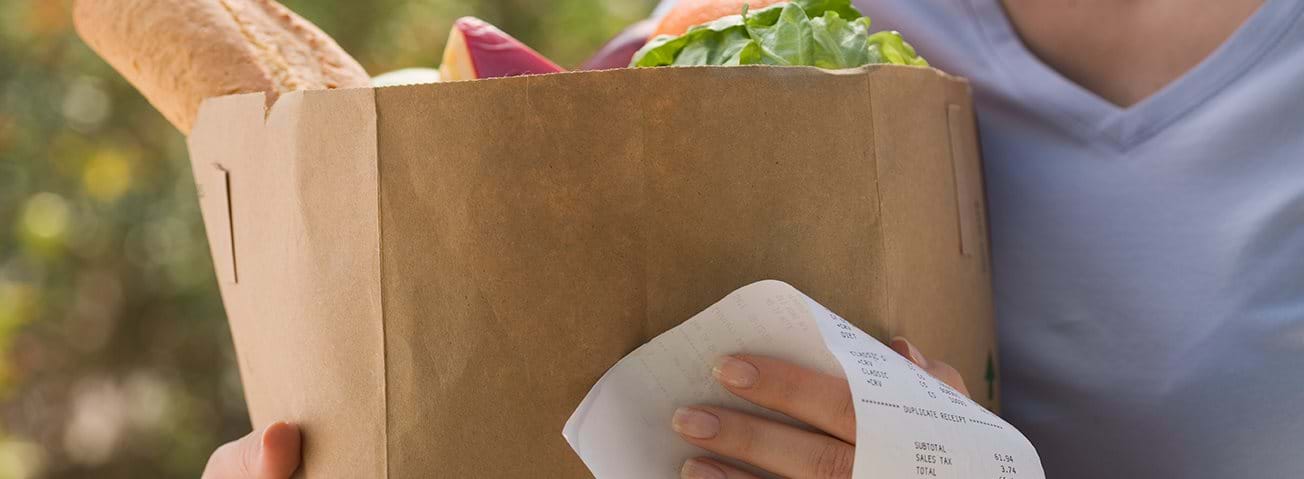 Photo of woman holding bag of groceries and receipt.