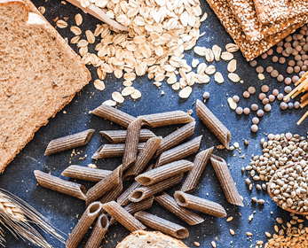 Photo of various whole grain products including bread, crackers, pasta, wheat, oats, and brown rice.