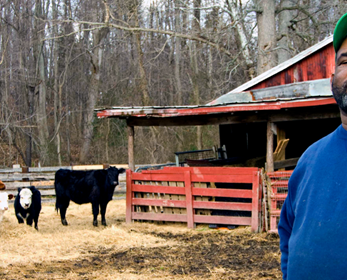 Photo of an African-American man with a barn and cattle in the background.