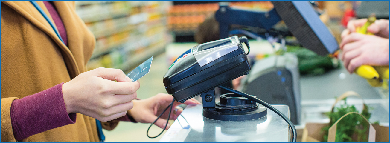 Photo of a woman using a credit/debit card at a grocery store checkout aisle. 