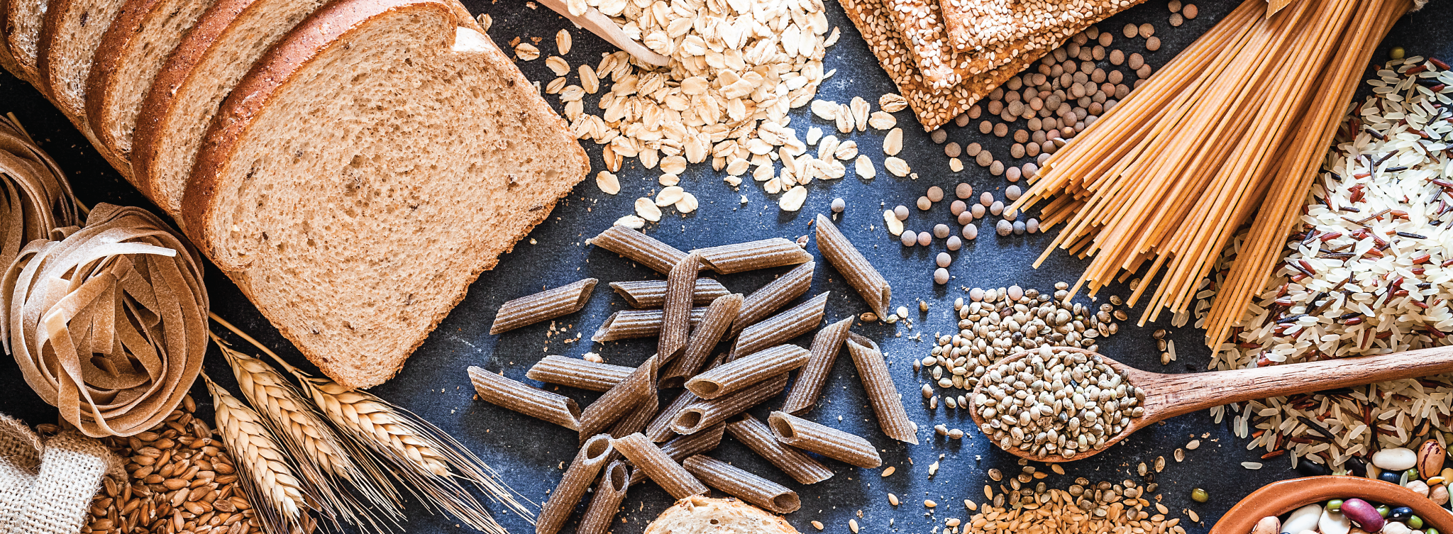 Photo of various whole grain products including bread, crackers, pasta, wheat, oats, and brown rice.