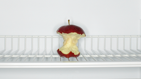 A picture of a mostly eaten apple in an otherwise empty refrigerator. 