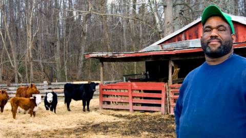 Photo of an African-American man with a barn and cattle in the background.