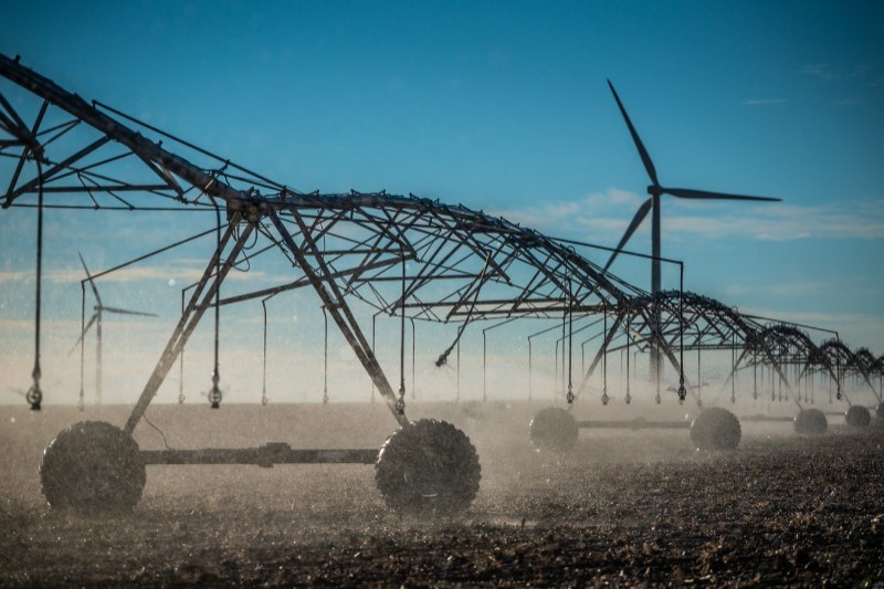 Photo of an irrigation pivot with windmills in the background