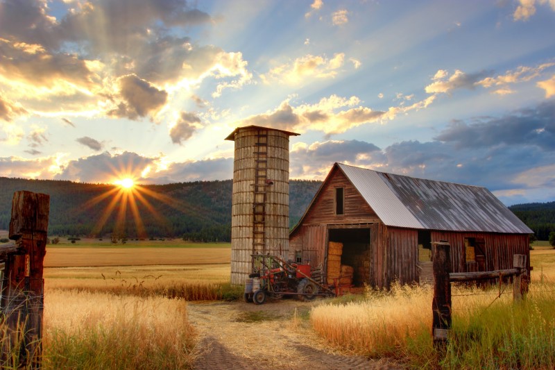 Photo of a barn and silo with the sunset in the background